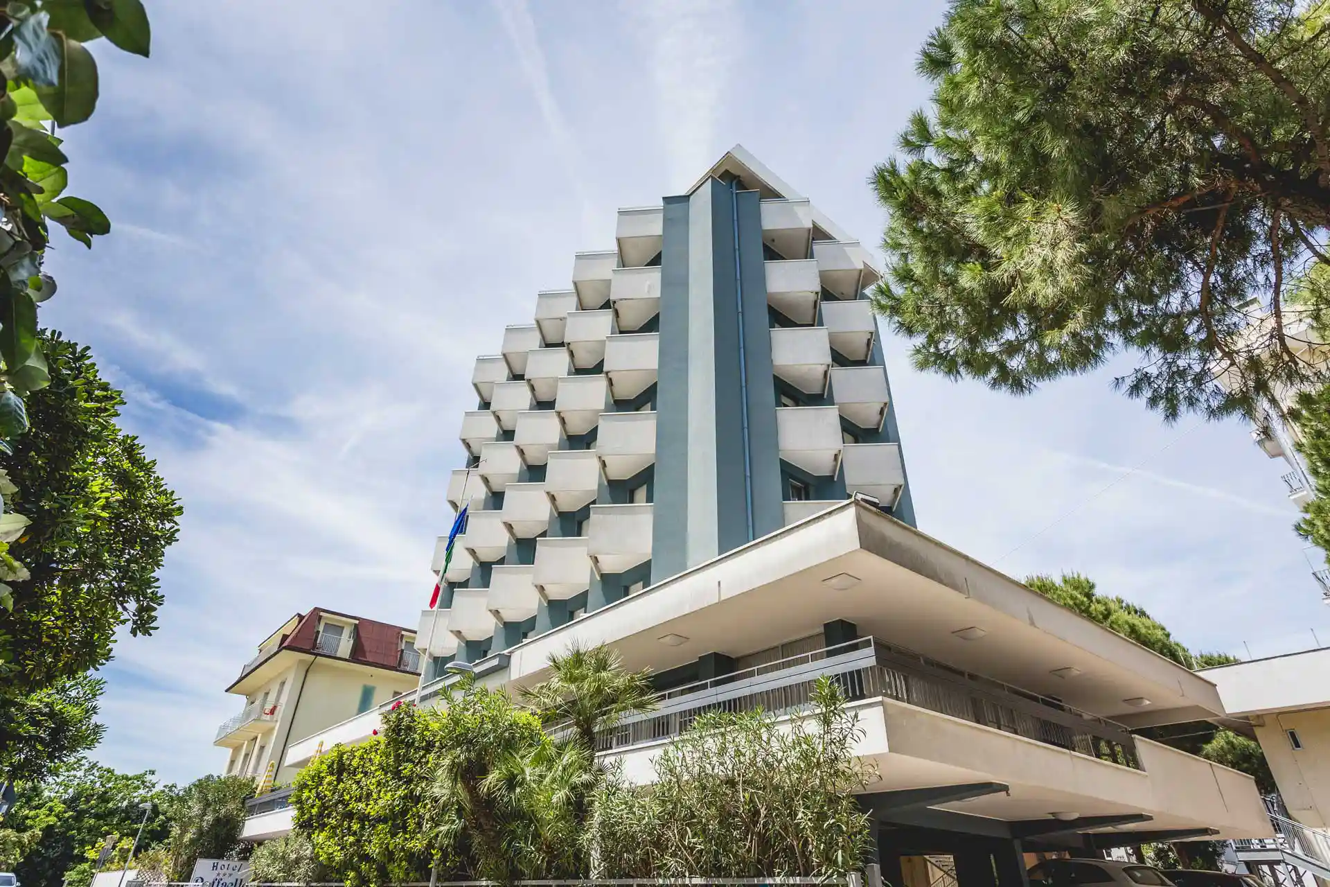 Ein modernes Hotelgebäude mit Balkonen und umgeben von Bäumen unter einem klaren Himmel.