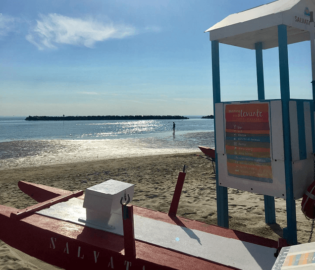 Strand mit Rettungsboot und einem Turm im Vordergrund, im Hintergrund das Meer.