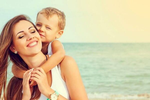 Madre e figlio sorridenti si abbracciano sulla spiaggia.