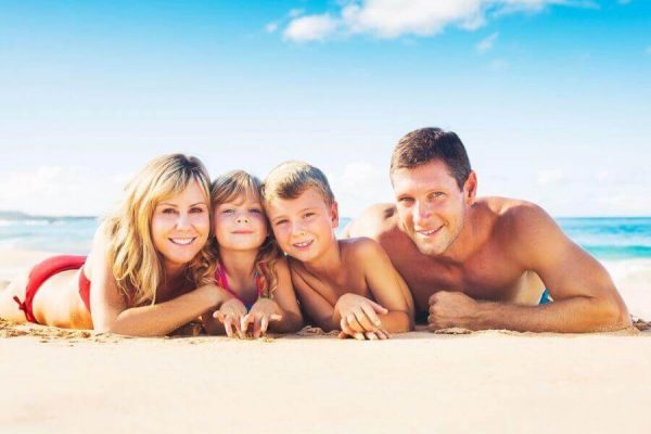 Famiglia sorridente sdraiata sulla spiaggia sotto un cielo sereno.